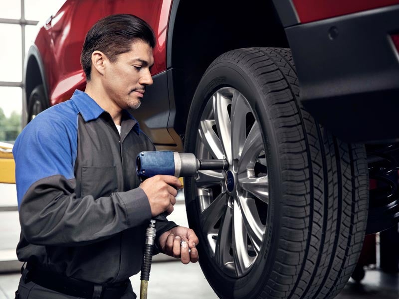 Technician rotating tires on a vehicle to ensure even wear.