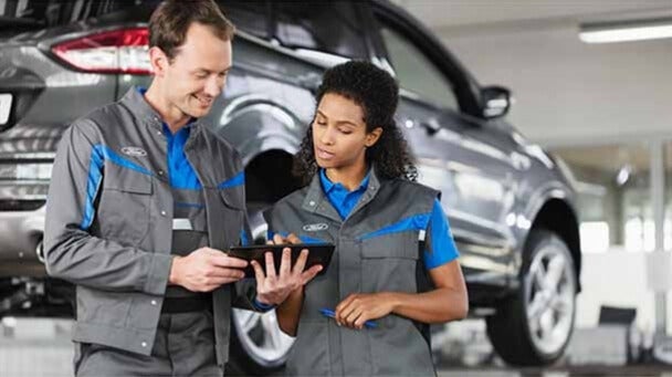 Technician using a tablet-based diagnostic tool to scan a vehicle's onboard computer system.